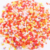 A pile of colorful polymer clay sprinkles mix in various shades of red, orange, pink, and yellow with small heart shapes and 