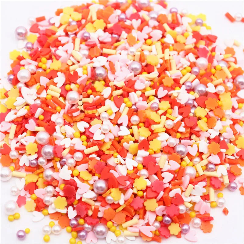 A pile of colorful polymer clay sprinkles mix in various shades of red, orange, pink, and yellow with small heart shapes and 