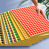 A hand is stacking colorful round self-adhesive dot labels in various sizes and colors on a light blue background.
