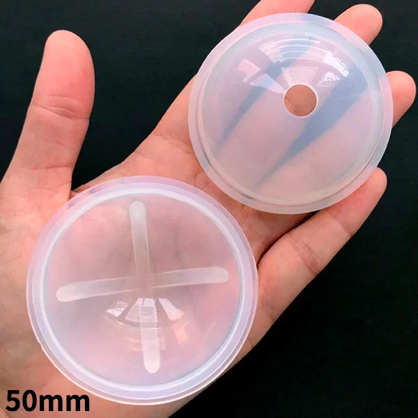 A hand holds two clear silicone molds for resin crafting, one disc and one flat circle.