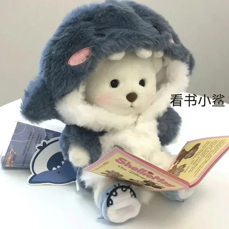 A fluffy gray and white teddy bear plush toy wearing a dress, displayed next to a booklet.