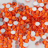A close-up of small, round, faceted orange glass crystal flatback rhinestones scattered on a white surface.