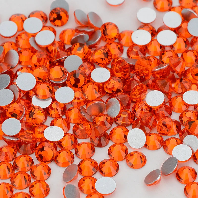 A close-up of small, round, faceted orange glass crystal flatback rhinestones scattered on a white surface.