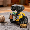 A yellow and gray minifigure-style vehicle built from building blocks with large black eyes and a green plant on a gray fabri