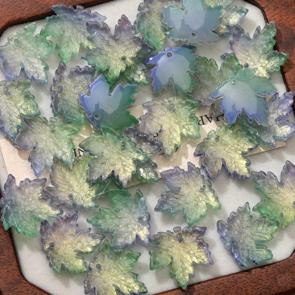 A collection of translucent green and blue maple leaf glass beads for DIY jewelry making.