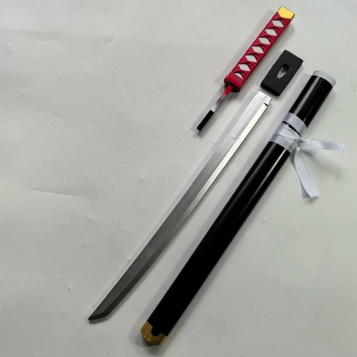 A long katana prop with a red checkered grip and a black sheath is displayed on a white background.