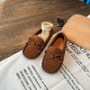 A pair of brown girls' moccasins with bow details resting on a white paper.