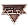 A bronze enamel pin featuring the text The Legend of Zelda in a stylized triangle shape.