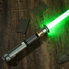 Accessoire d'épée laser avec une lame verte luminescente posé sur une surface en bois sombre.