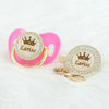 A pink silicone pacifier clip set featuring a rose gold crown charm and a personalized lariisa name plate.