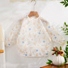 A white waterproof baby bib with long sleeves featuring a pattern of small yellow and blue birds.