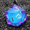 A handmade resin D20 die with a large blue and purple liquid swirl, viewed from above on black gravel.