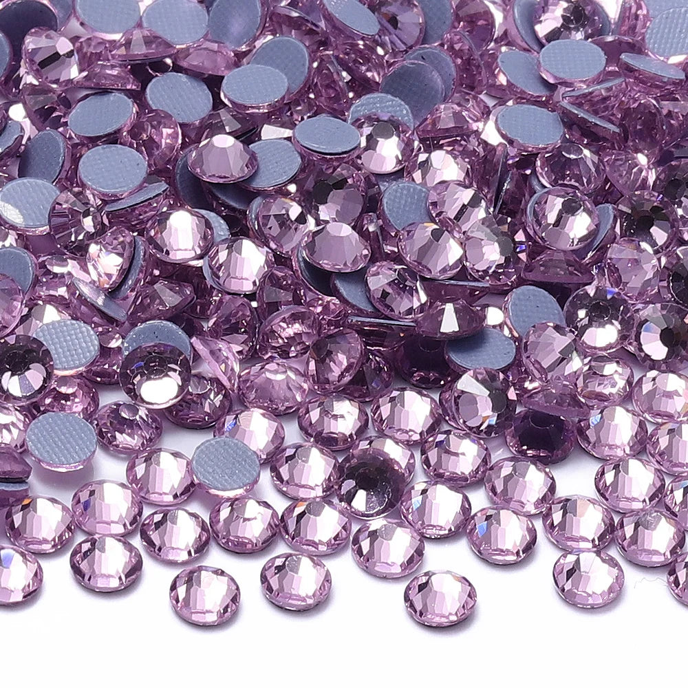 A close-up view of various shades of pink and purple glass crystal rhinestones scattered on a white surface.