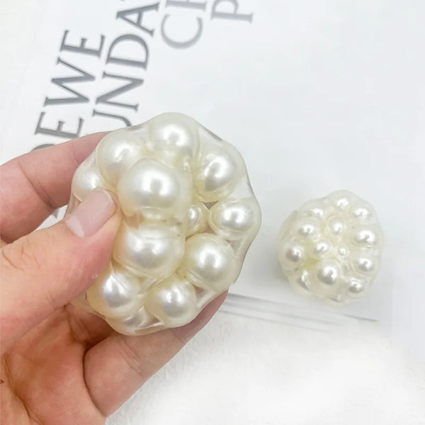 A hand holds a cluster of white pearl beads used for stress relief or squishy balls.