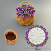 A hand-crocheted mat featuring purple and yellow flowers on a white background, shown next to a small woven basket.