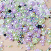 A scatter of mixed resin rhinestone pearls in shades of pink, purple, and green on a light wooden surface.