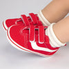 A pair of red and white striped baby canvas sneakers with white fabric cuffs is shown on a person's foot.