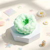 A pale green squishy sensory stress ball resting on a white block with small star-shaped fidget toys nearby.