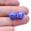 Two small blue glass charm pendants shaped like flowers are held between fingers.