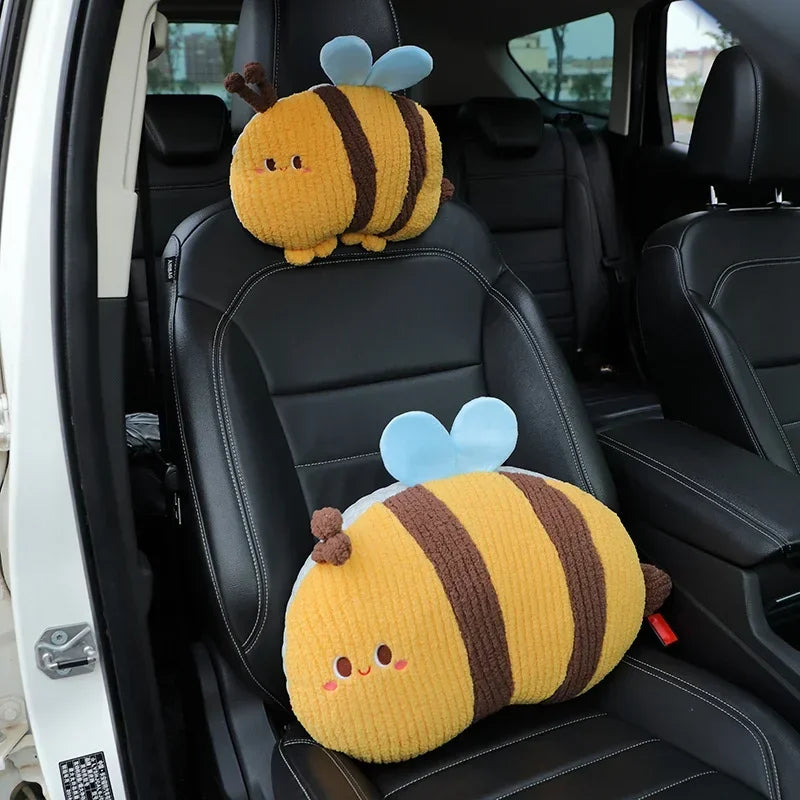 A yellow plush bee lumbar support pillow with brown stripes and blue wings is placed on a black car seat.