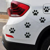 Rear view of a white car with black paw print vinyl stickers on the body and bumper.