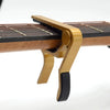 A close-up view of a brass guitar capo mechanism with a wooden neck and strings.