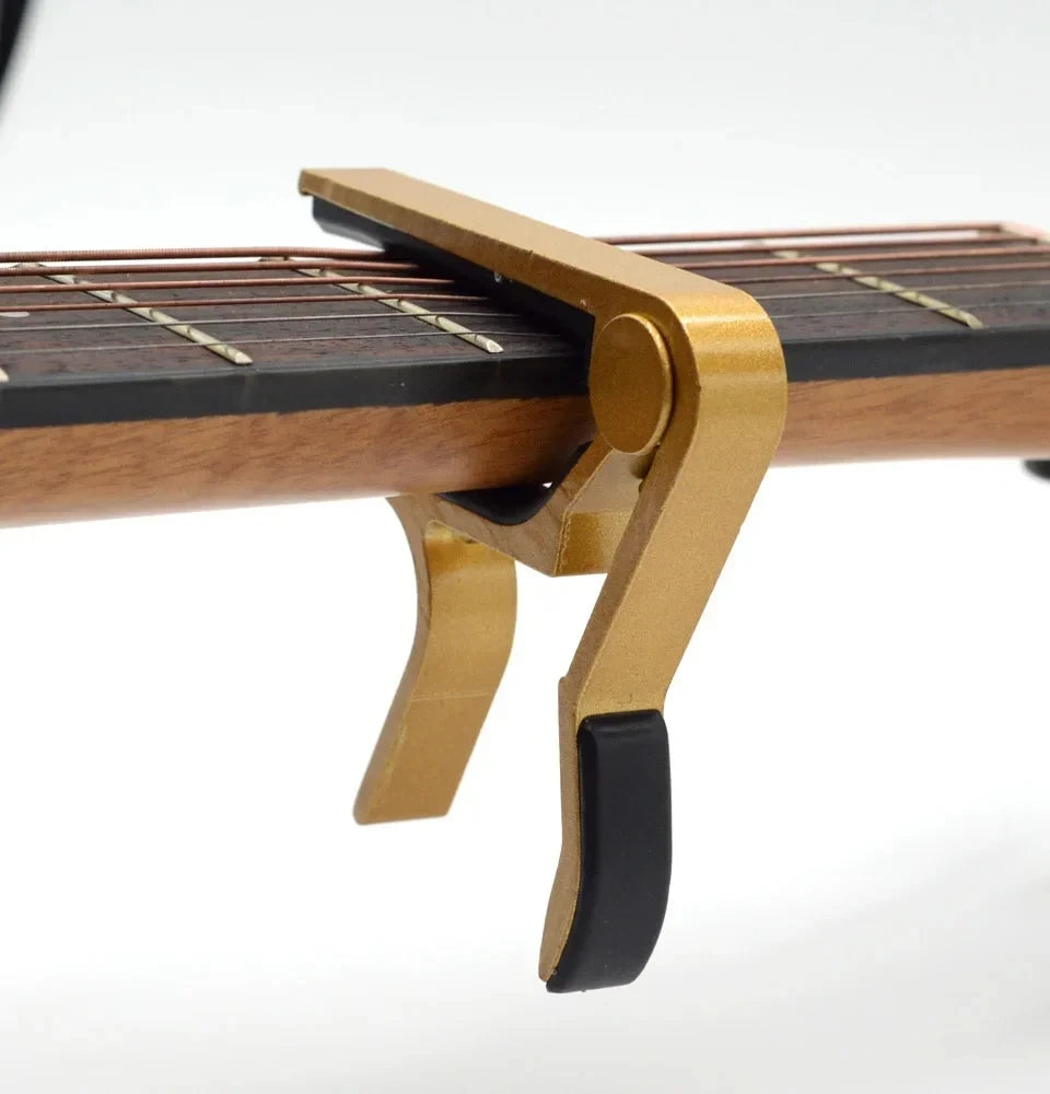 A close-up view of a brass guitar capo mechanism with a wooden neck and strings.
