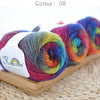 Spool of hand-dyed rainbow merino wool yarn in various vibrant colors resting on a wooden board.