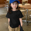 A young girl wearing a blue cap and a black crew neck t-shirt stands in a cafe setting.