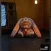 A purple and orange plush doll with long floppy ears sits on a dark surface.