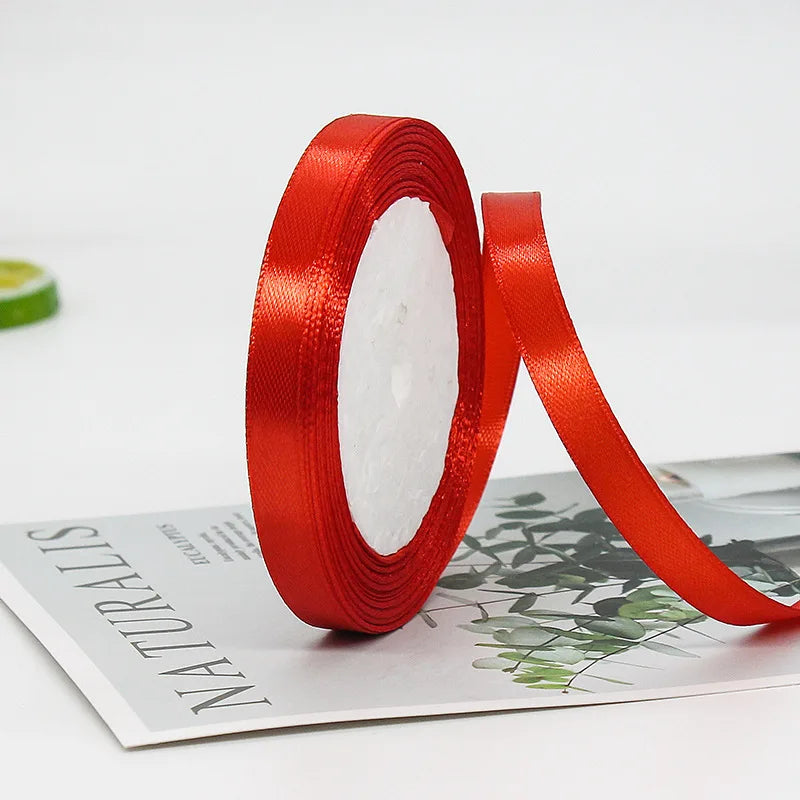 A roll of red satin ribbon used for gift wrapping or crafts is shown lying on a white surface.