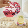 A hand holds a pink diamond art coaster featuring a red vintage truck and hearts, with a glass of lemonade nearby.