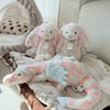 Pink and white rainbow dragon plush pillow with soft fur resting on a striped fabric.
