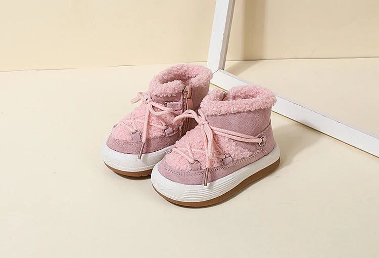 A pair of pink baby winter snow boots with plush lining and white rubber soles resting on a light surface.