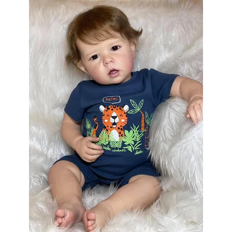 A baby doll wearing a dark blue onesie with an orange tiger design sitting on a white fluffy surface.