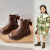 A young girl models brown ankle boots with bow-knot details and a side zipper, standing next to a pair of boots.