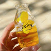 A hand holds a clear glass bottle filled with yellow liquid and floating fruit pieces, used as a drink cup toy.