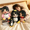 A plush toy featuring a black and white penguin character is resting on a light-colored bed with books nearby.