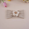 A beige knitted elastic headband with a white flower detail is shown on a light pink background.