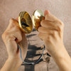 Hands holding handcrafted brass Tingsha cymbals with eight auspicious symbols