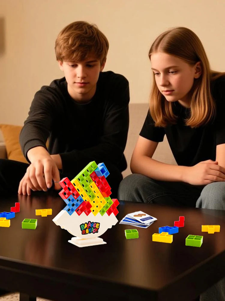 Two children are playing with a colorful balance stacking tower game on a dark table.