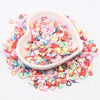 Pink and multicolored polymer clay sprinkles in a white dish scattered on a white background