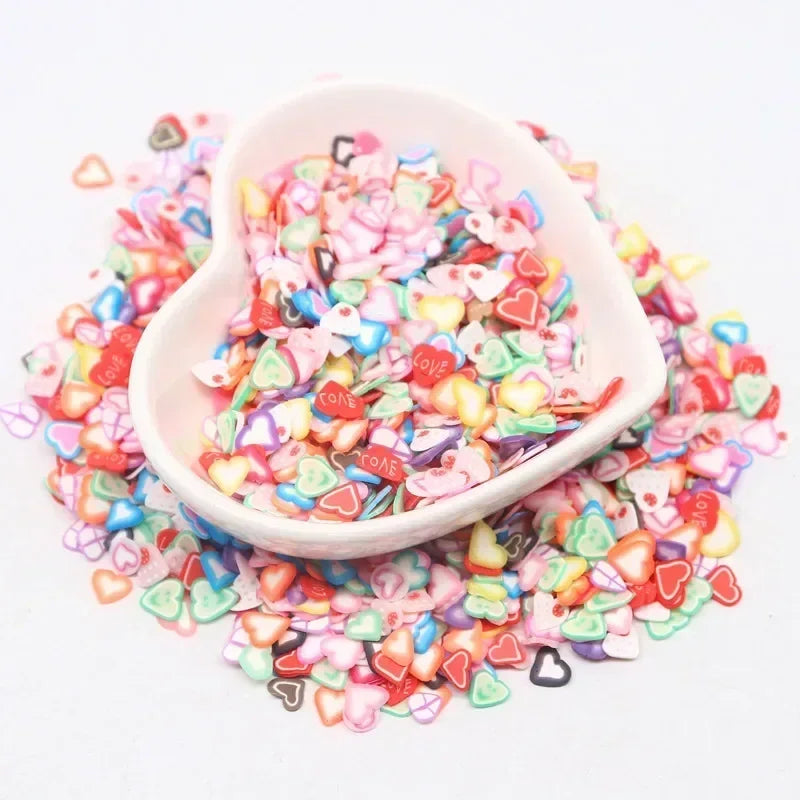 Pink and multicolored polymer clay sprinkles in a white dish scattered on a white background
