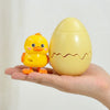 A hand holds a yellow egg-shaped wind-up bouncing chick toy.