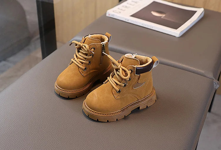 A pair of tan kids' winter leather boots with laces and a brown cuff resting on a gray surface.