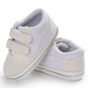 A pair of light beige canvas baby sneakers with a striped design shown from the side.