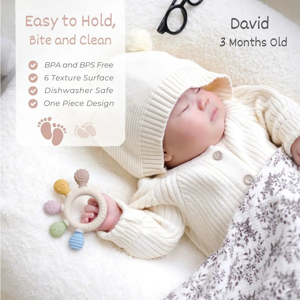 A newborn baby is sleeping peacefully while holding a silicone baby teether with chew beads.