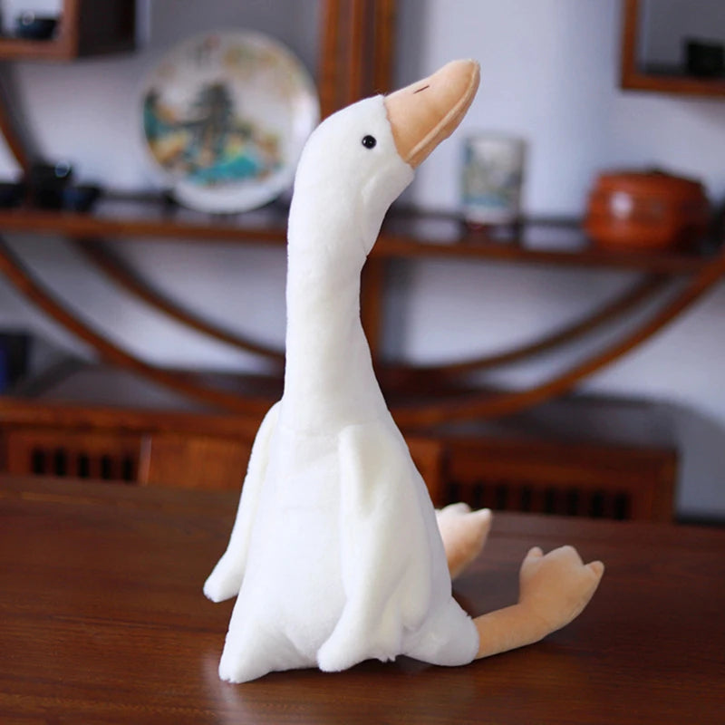 A white long neck goose plush doll with orange feet sitting on a wooden surface.