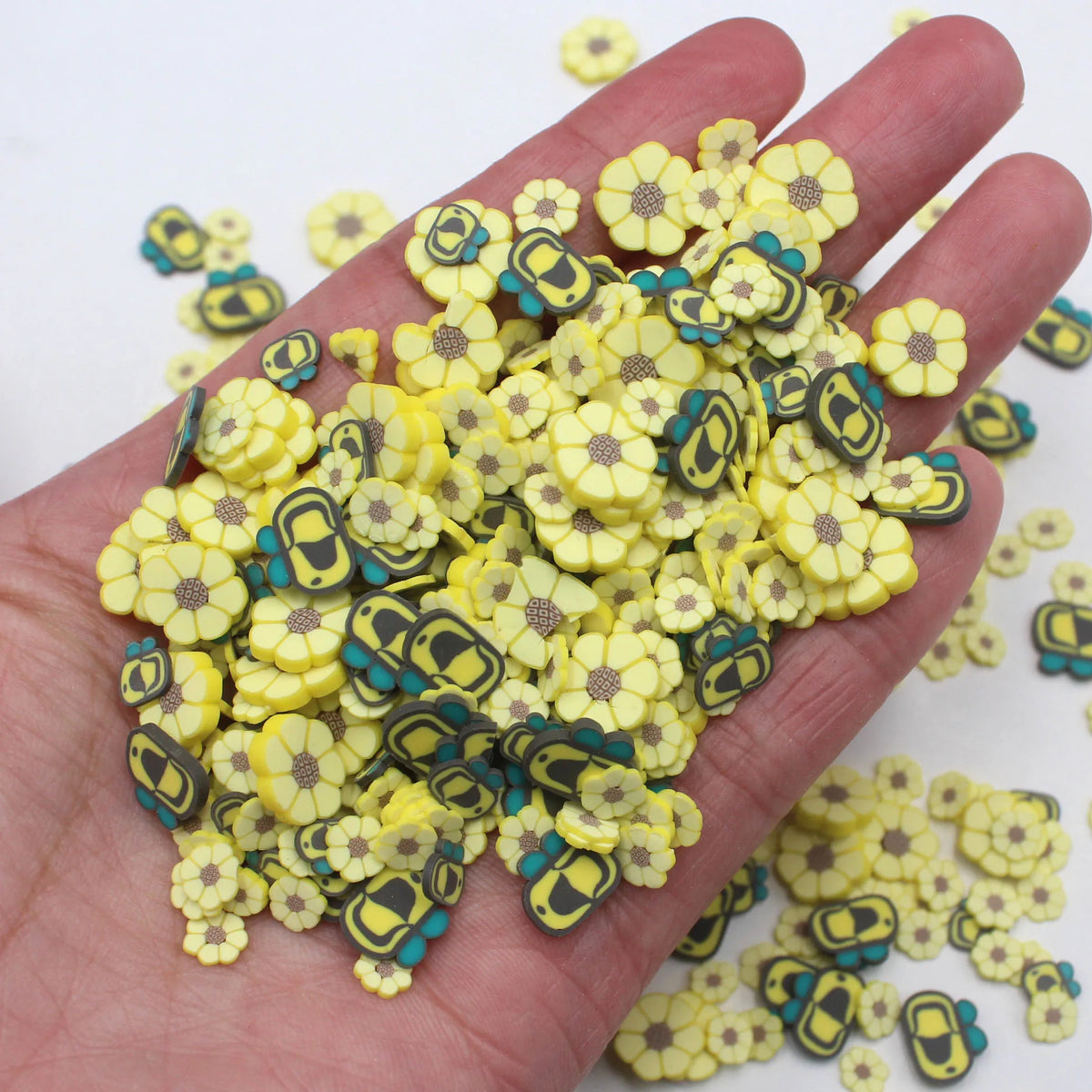 A hand holds a pile of assorted polymer clay sunflower and bee slices for crafts in yellow and green colors.