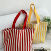 Un sac fourre-tout en toile à épaules rayé rouge et blanc est exposé sur une surface blanche.